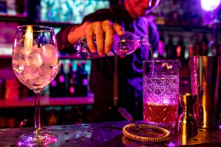 Close up of professional barman finishes preparation of alcoholic cocktail in multicolored neon...