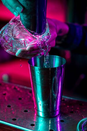 Close up of professional barman finishes preparation of alcoholic cocktail in multicolored neon lightの写真素材