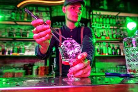 Close up of professional barman finishes preparation of alcoholic cocktail in multicolored neon light, gives it to client. Entertainment, drinks, service concept. Modern bar, trendy neoned colors.の写真素材