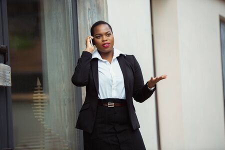 Talking on phone. African-american businesswoman in office attire smiling, looks confident and happy, busy. Finance, business, equality and human rights concept. Beautiful young feme model, successful.の写真素材