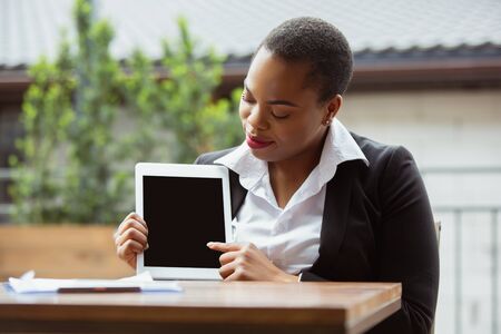 Showing blank tablet screen. African-american businesswoman in office attire smiling, looks confident, busy. Finance, business, equality, human rights concept. Beautiful young feme model, successful.の写真素材