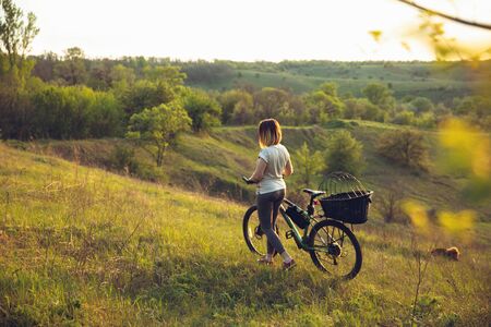 Young woman having fun near countryside park, riding bike, traveling with companion spaniel dog. Calm nature, spring day, positive emotions. Sportive, active leisure activity. Walking together.の写真素材