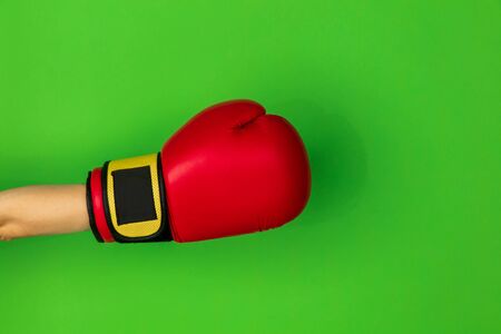 Hand in boxing, boxers red glove isolated on green studio background with copyspace. Kicking, holding, fighting at side. Negative space for your advertising. Sport, ad, activity, competition.の写真素材