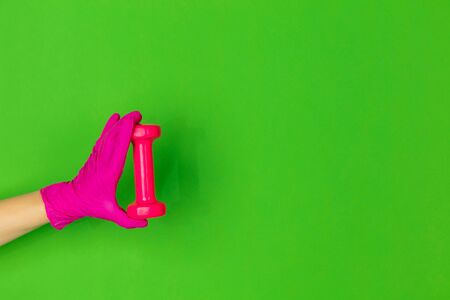 Hand in pink protective glove wth dumbbell isolated on green studio background with copyspace. Gesturing, holding, presenting things. Negative space for your advertising. Showing, pointing.の写真素材
