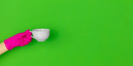Hand in pink protective glove with coffee cup isolated on green studio background with copyspace....