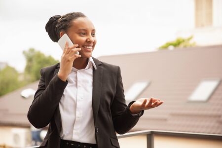 Important call. African-american businesswoman in office attire smiling, looks confident and happy, busy. Finance, business, equality and human rights concept. Beautiful young feme model, successful.の写真素材