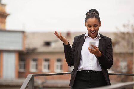 Talking phone, astonished. African-american businesswoman in office attire smiling, looks confident happy, busy. Finance, business, equality and human rights concept. Beautiful young model, successful.の写真素材