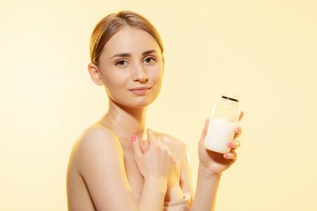 Close up of beautiful young woman massaging skin with moisturizer yellow background. Concept of cosmetics, makeup, natural and eco treatment, skin care. Shiny and healthy skin, fashion, healthcare.の写真素材