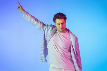 Young caucasian musician in casual dancing on gradient blue background in neon light. Concept of...