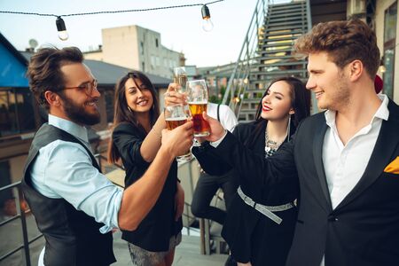 Success. Young people celebrating, look happy, have party at office or bar. Men and women drinking alcohol, talking, laughting. Holidays, weekend, business and finance, friendship concept. Teambuilding.の写真素材