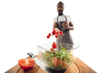 Amazing african-american man preparing unbelievable food with action, details and bright emotions, professional cook isolated on white studio background. Modern kitchen, artwork. Close up, wide angle.の写真素材