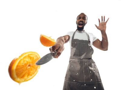 Amazing african-american man preparing unbelievable food with action, details and bright emotions, professional cook isolated on white studio background. Modern kitchen, artwork. Close up, wide angle.の写真素材