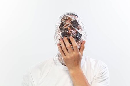 Male face covered with oilcloth, cellophane and unhealthy food, hard to breathe. People lost their faces, cant notice the environmental pollution made by themself. Garbage, problem, breathing.の写真素材