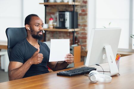 Thumb up. Young man, businessman working in office, looking on blank black computer screen, monitor. Copyspace for your ad. Finance, business, work, gadgets and tech concept. Freelance, remote worker.の写真素材
