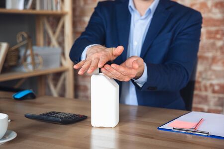 Disinfecting hands with sanitizer. Close up young man, manager return to work in his office after quarantine, feels happy and inspired. Coming back to normal life. Business, finance, emotions concept.の写真素材