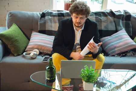 Reviewing document. Man in pajama and jacket working on a computer, laptop. Remote office during...