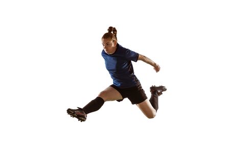 Young female soccer or football player with long hair kicking ball for the goal in flight, jumping high on white studio background. Concept of healthy lifestyle, professional sport, motion, movement.の写真素材