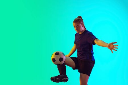 Young female soccer or football player with long hair in sportwear kicking ball for the goal, training on gradient background, neon. Concept of healthy lifestyle, professional sport, motion, movement.の写真素材