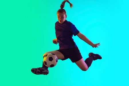 Young female soccer or football player with long hair in sportwear kicking ball for the goal in jump on gradient background, neon. Concept of healthy lifestyle, professional sport, motion, movement.の写真素材