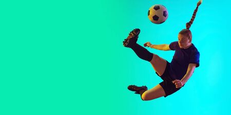 Young female soccer or football player with long hair in sportwear kicking ball for the goal in jump on gradient background, neon. Concept of healthy lifestyle, professional sport, motion, movement.の写真素材