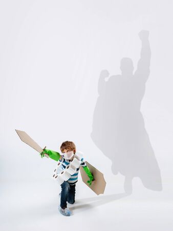 Superhero in shadow of ordinary people - modern superheros concept, respect and admiration. Boy with sword keep fighting with coronavirus like warrior, setting good example. Inspiring others.の写真素材