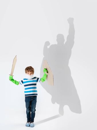 Superhero in shadow of ordinary people - modern superheros concept, respect and admiration. Boy with sword keep fighting with coronavirus like warrior, setting good example. Inspiring others.の写真素材