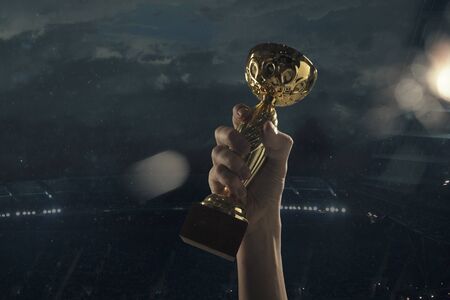 Dream comes true. Award of victory, male hands tightening the golden cup of winners against cloudy dark sky. Sport, competition, championship, winning, achieving the goal. Prize for success and honor.の写真素材