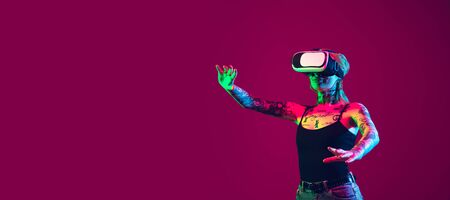 Playing with VR-headset. Young caucasian woman on purple studio background in neon light. Beautiful...