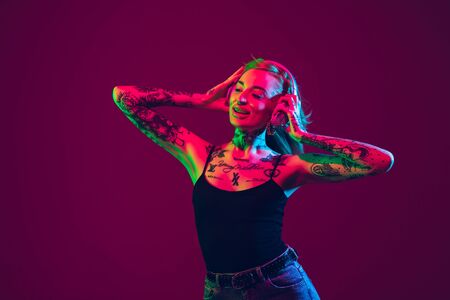 Listening to music, dancing with wireless headphones. Portrait of young caucasian woman on purple background in neon light. Human emotions, facial expression, sales, ad concept. Freaks culture.の写真素材