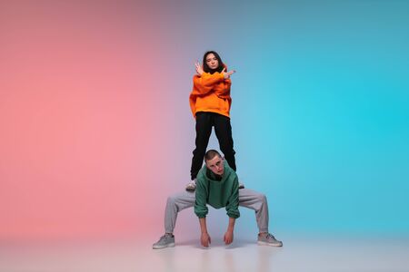 Boy and girl dancing hip-hop in stylish clothes on colorful gradient background at dance hall in neon. Youth culture, movement, style and fashion, action. Fashionable bright portrait. Street dance.の写真素材