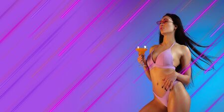 Beautiful woman in swimsuit with cocktail. Creative portrait with copyspace. Neon colored portrait with neon lines, flyer, proposal. Motion, youth culture concept. Contemporary art, modern design.の写真素材