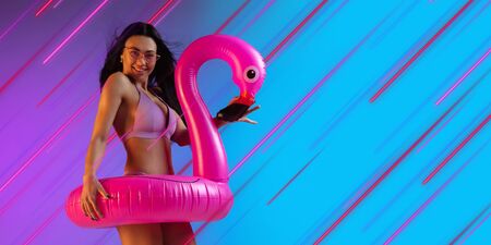 Beautiful woman in swimsuit with flamingo. Creative portrait with copyspace. Neon colored portrait with neon lines, flyer, proposal. Motion, youth culture concept. Contemporary art, modern design.の写真素材