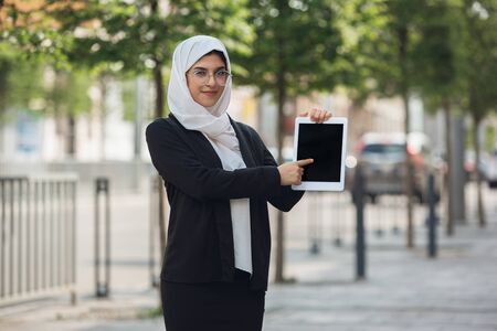 Pointing on tablet screen. Beautiful muslim successful businesswoman portrait, confident happy CEO, leader, boss or manager. Using devices, gadgets, working on the go, looks busy. Inclusive, diversity.の写真素材