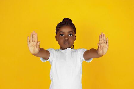 Rejecting, stopping. Little african-american girls portrait on yellow studio background. Cheerful, serious kid. Concept of human emotions, facial expression, sales, ad. Copyspace. Looks cute.の写真素材