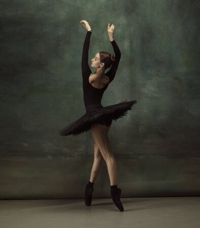 Art motion. Graceful classic ballerina dancing, posing isolated on dark studio background. Elegance black tutu. Grace, movement, action and motion concept. Looks weightless, flexible. Fashionable.の写真素材