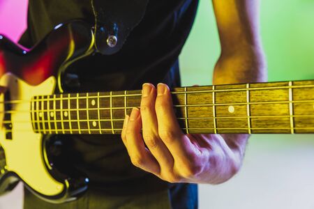 Close up musician hands playing bass guitar on gradient studio background in neon light. Concept of music, hobby, festival. Colorful portrait of modern artist. Inspired, impressive improvising.の写真素材