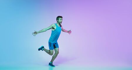 The first, winner. Portrait of young caucasian man running, jogging on gradient studio background in neon light. Professional sportsman training in motion. Sport, wellness, activity, concept. Flyer.の写真素材