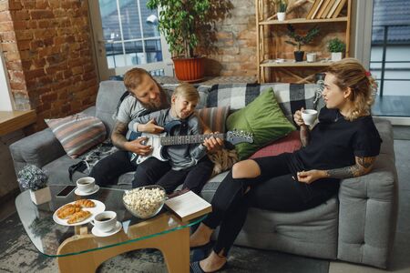 Happy family at home spending time together. Having fun, look cheerful and lovely. Mother, father and son playing guitar, talking, singing. Childhood, domestic life, togetherness concept.の写真素材