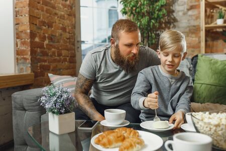 Happy family at home spending time together. Having fun, look cheerful and lovely. Father and son eating sweets, talking, laughting. Childhood, domestic life, togetherness, happiness concept.の写真素材