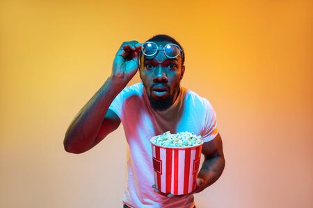 Shocked, disbelief. African-american mans modern portrait on gradient orange studio background in neon light. Beautiful afro model. Concept of emotions, cinema, facial expression, sales, ad.の写真素材