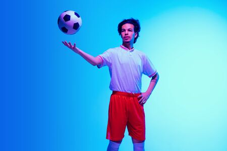 Passioned for game. Football or soccer player on gradient blue studio background in neon light - motion, action, activity. Concept of sport, competition, winning, action, motion, overcoming. Copyspace.の写真素材