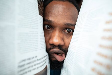 In papers, magazines, books. African-american man looking for job in unusual places at his home. Crazy, funny way to find career and going up. Concept of crisis, unemployment, finance, business.の写真素材