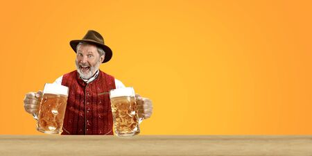 Delighted senior man with beer dressed in traditional Austrian or Bavarian costume holding mug of beer at pub or studio. The celebration, oktoberfest, festival, drinking concept. Flyer with copyspace.の写真素材