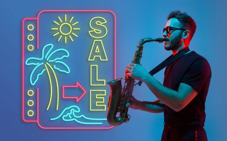 Young jazz musician playing the saxophone on gradient studio background in neon light neon sign SALE. Concept of music, hobby, festival. Joyful inspired artist, flyer. Summertime, sale, vacation.の写真素材