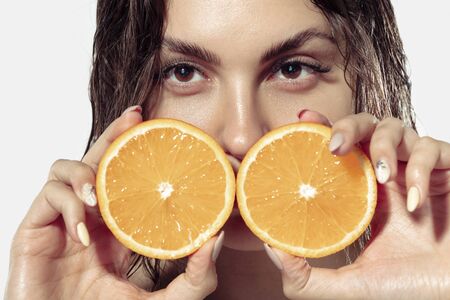 Close up beautiful young woman with orange slices on white background. Concept of cosmetics, makeup, natural and eco treatment, skin care. Shiny and healthy skin, fashion, healthcare. Copyspace.の写真素材