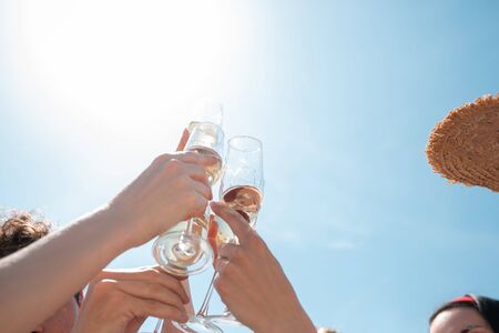 Close up clinking, cheers. Seasonal feast at beach resort. Group of friends celebrating, resting, having fun in sunny summer day. Look happy and cheerful. Festive time, wellness, holiday, party.の写真素材