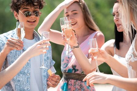 Cheers, clinking glasses. Seasonal feast at beach resort. Group of friends celebrating, resting, having fun in sunny summer day. Look happy and cheerful. Festive time, wellness, holiday, party.の写真素材