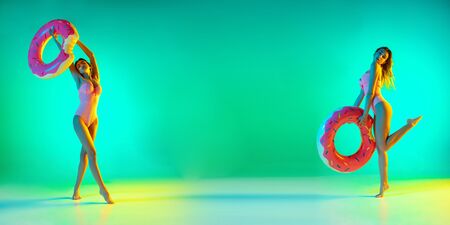 Fashion portrait of seductive girl in stylish swimwear on green background in neon. Summertime, beach season. Woman with sportive body. Resort, vacation, holidays concept. Flyer, copyspace for ad.の写真素材