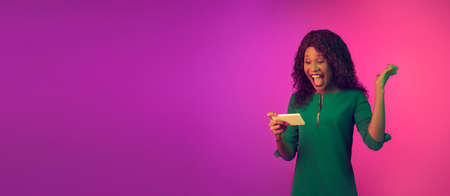Winner, crazy shocked. African-american young woman on gradient pink background in neon light. Beautiful female model. Concept of human emotions, facial expression, sales, ad. Flyer with copyspace.の写真素材