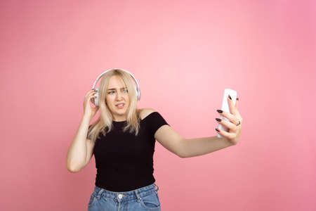 Taking selfie. Portrait of young caucasian woman with bright emotions on coral pink studio...